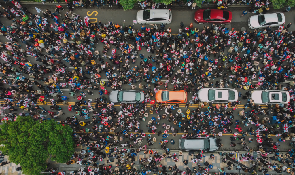 Aerial view of a crowd of protestors covering a road with cars parked.